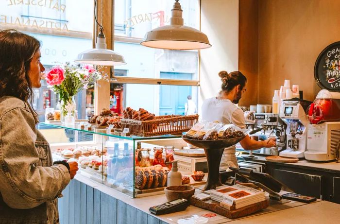 A customer waits as a staff member prepares an order behind a display of pastries.