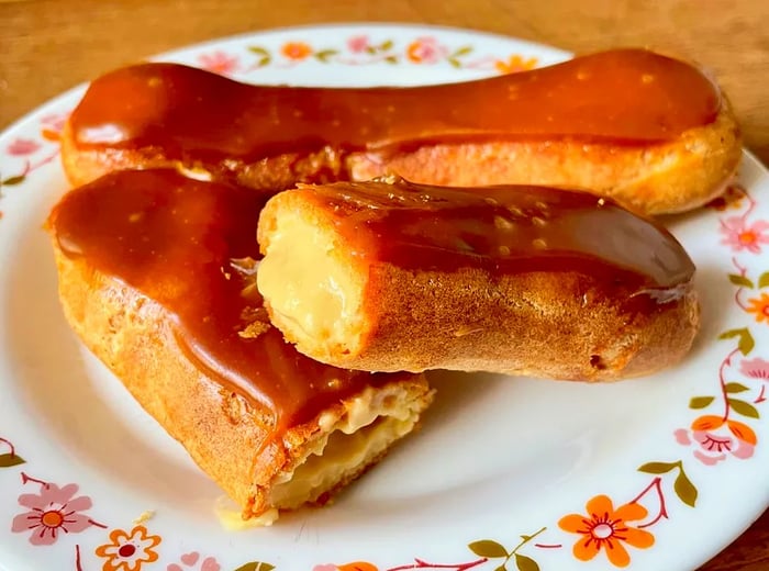 A plate showcasing two eclairs, one topped with a glossy chocolate glaze and the other cut open to reveal its creamy filling.