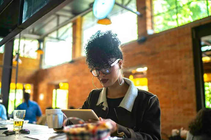 A woman reads on her tablet while enjoying a meal alone at a restaurant.