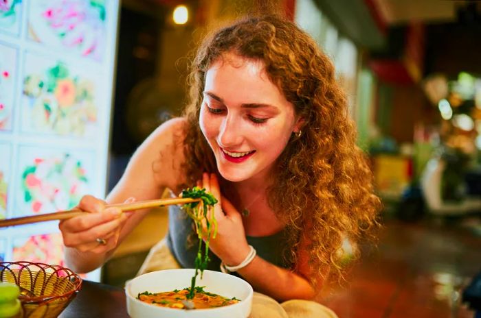 A woman enjoys noodles at a restaurant.