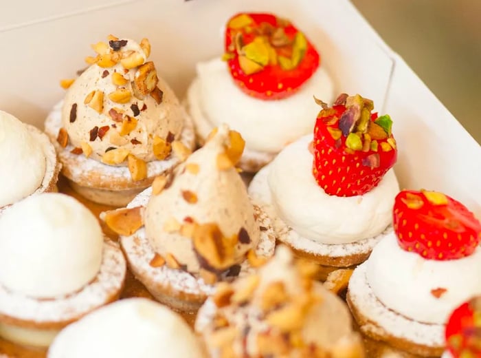 A box of sablés adorned with strawberries, chopped nuts, and a smooth creamy topping.