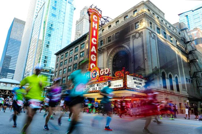 Participants in the Chicago marathon run past the Chicago Theater, with its iconic red and white marquee illuminated in the background.