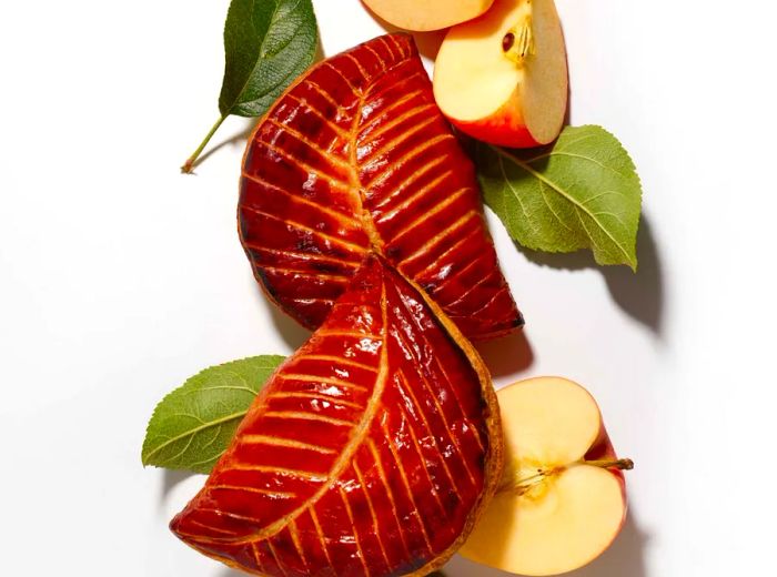 Aerial view of pastry shells resembling leaves, golden from the oven, alongside apple slices.