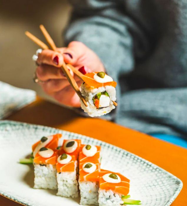 A diner lifts a piece of plant-based sushi roll with chopsticks above a plate.