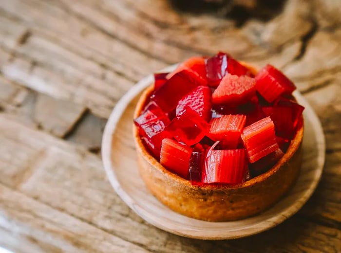 A tart topped with fresh rhubarb and jelly, elegantly presented on a wooden table.