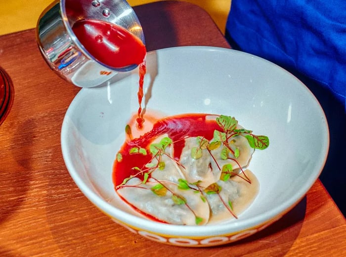 A server drizzles red sauce over dumplings garnished with fresh herbs.