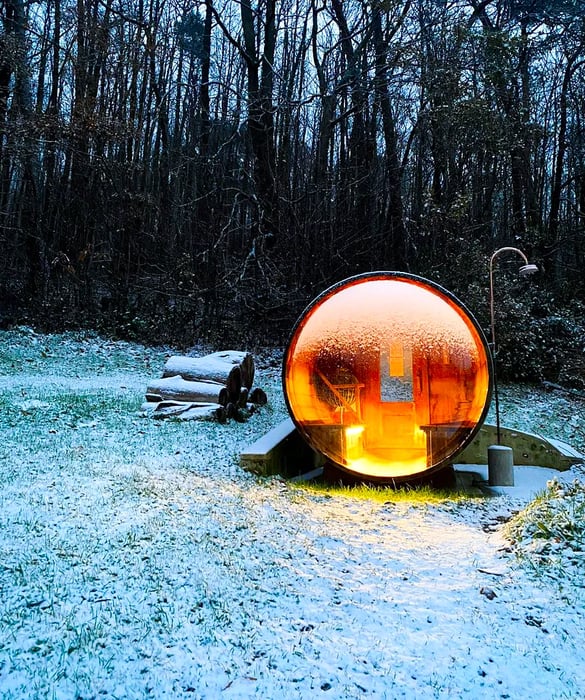 A cozy sauna features a large glass wall, set against a backdrop of a snowy forest.