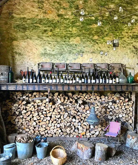 Wine bottles are neatly arranged on a ledge above neatly stacked firewood.