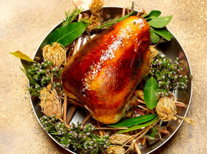 A beautifully roasted chicken surrounded by herbs and edible flowers in a pan.