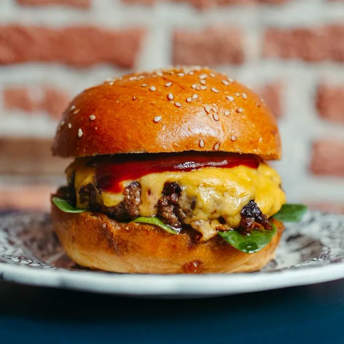 A neatly assembled cheeseburger positioned in front of a rustic exposed brick wall.