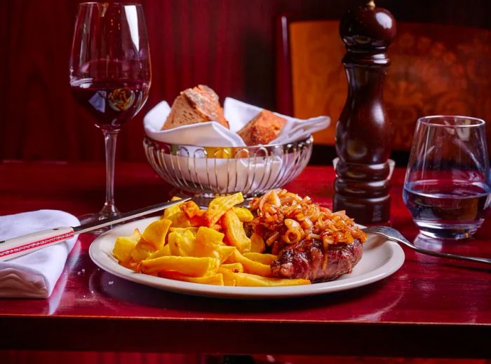 A serving of steak frites accompanied by wine and bread.