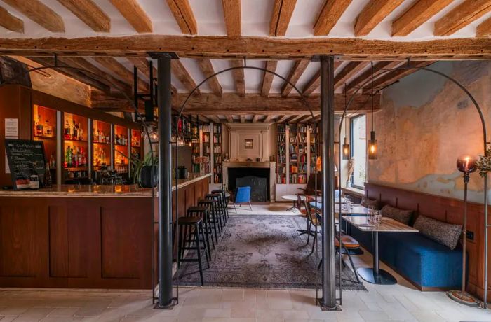 A view through several expansive wireframe arches into a dining area featuring a blue leather banquette on one side and a bar on the other, with a library visible in the background.