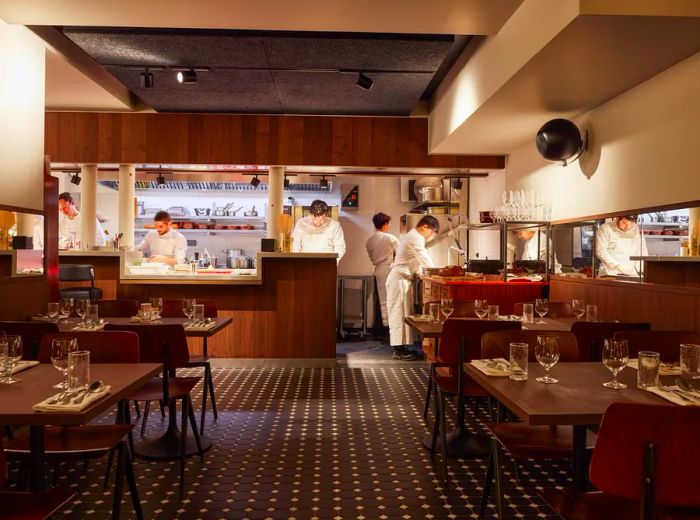 An empty dining room set up for service, featuring an open kitchen where chefs are hard at work.