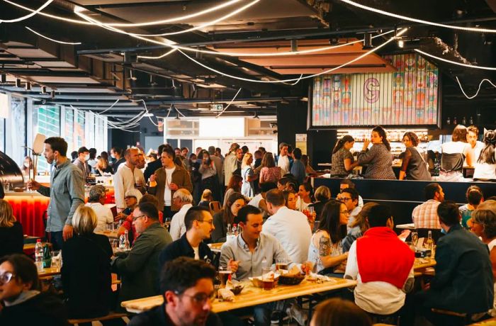 A bustling crowd enjoying their meals at communal tables within a food hall.