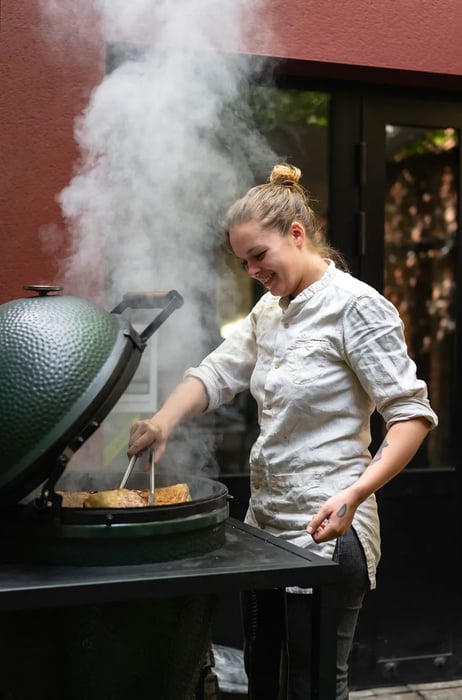 A chef tends to an outdoor grill, sending plumes of smoke into the air.