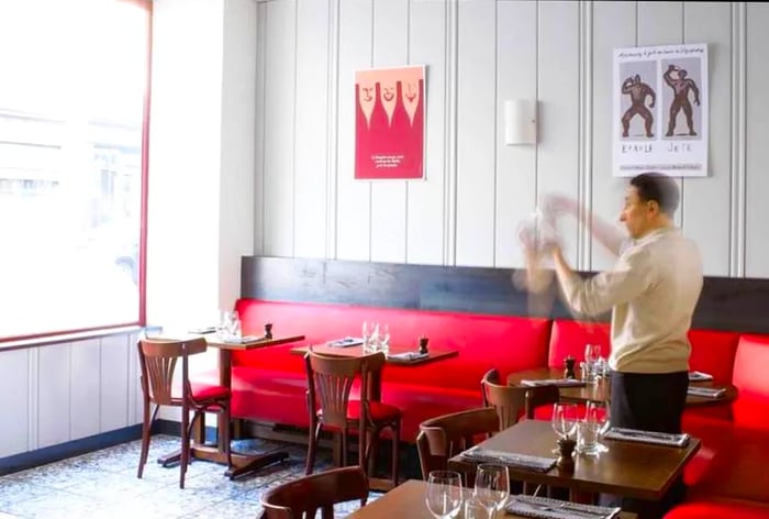 The dining room, adorned with wood walls and leather banquettes, is flooded with light through large windows that create a vibrant atmosphere.