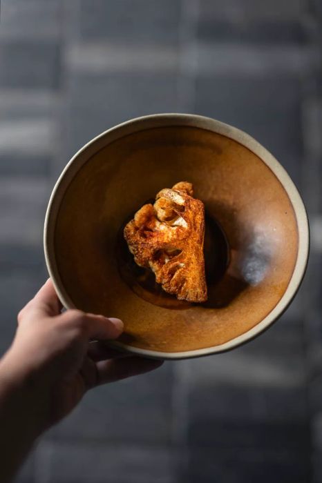 A quarter of cauliflower seasoned with spices in a brown bowl.