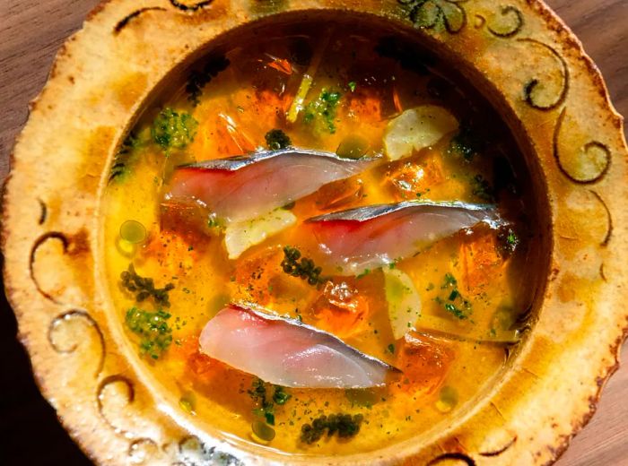 A beautifully crafted bowl showcasing slices of mackerel swimming in a rich, golden broth.