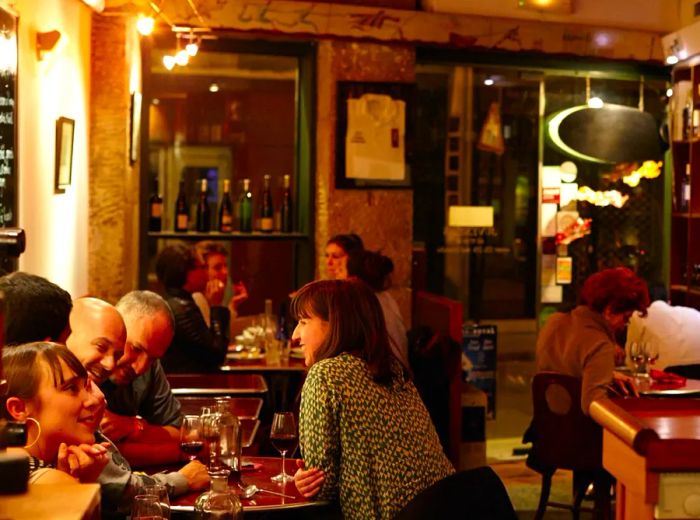 A snug dining area where guests are seated at intimate tables, with wine bottles adorning the walls.