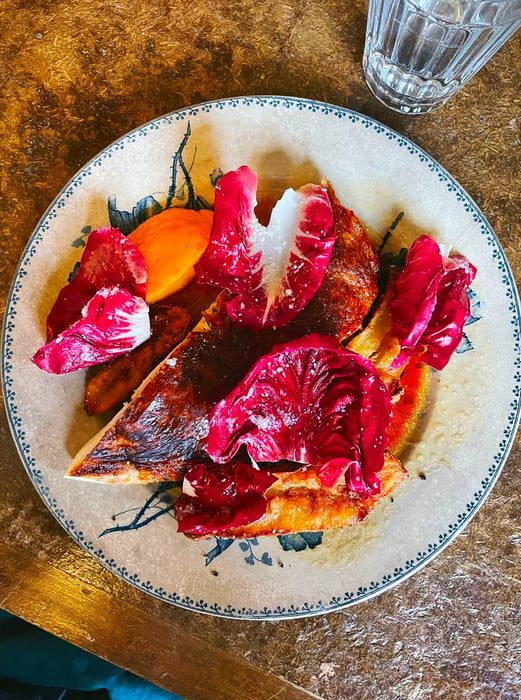 A close-up of a chicken breast with its skin, accompanied by vibrant purple radicchio leaves.