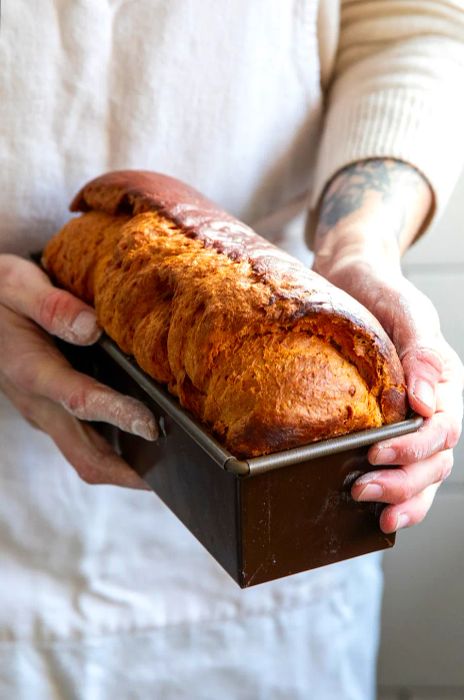 A person presents a loaf of bread in a pan.