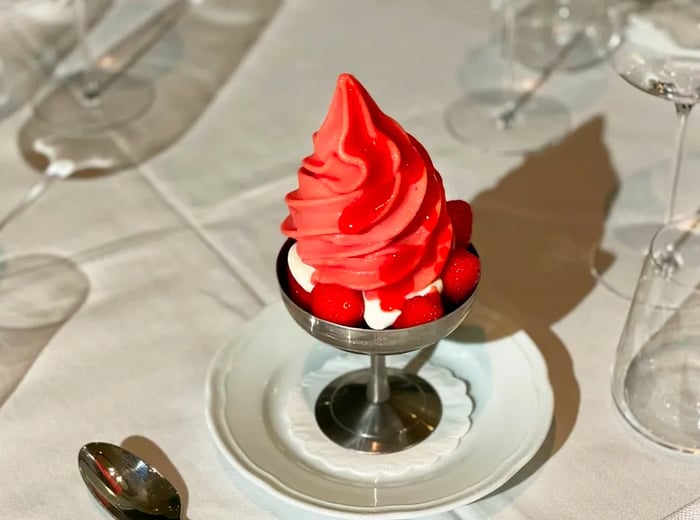 A tall, pink swirl of soft serve served in an elegant silver chalice.