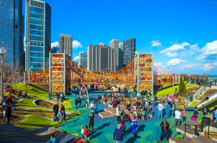 Families enjoying a spacious playground featuring a large wooden climbing structure and metal tube slides