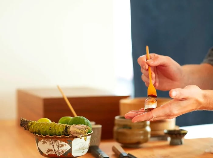 A sushi chef carefully brushes a flavorful sauce onto a piece of nigiri.