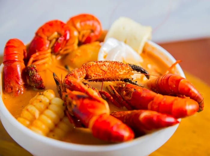 A rich soup featuring large red shrimp, corn, and a crab claw.