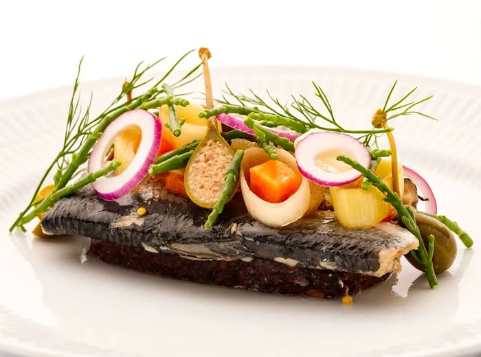 Smørrebrød adorned with dark fish, fresh vegetables, and sliced boiled eggs.