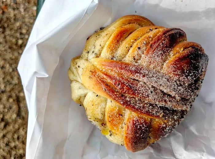 A close-up of a cardamom bun, dusted with sugar and nestled on a paper bag.