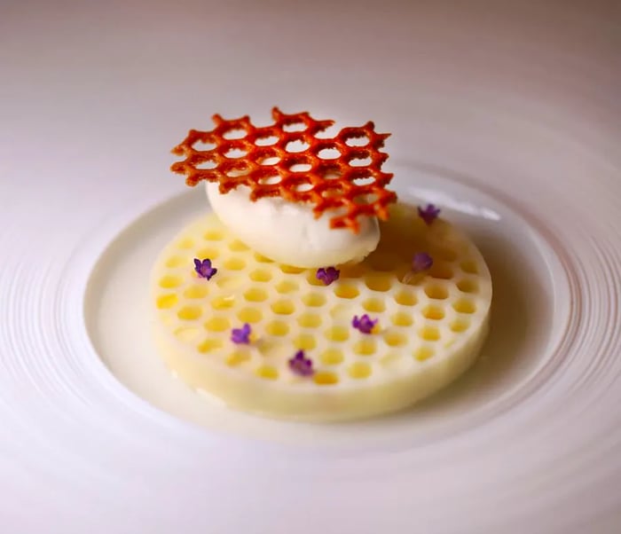 A delicate dessert resembling a thin waffle, topped with a cloud of cream and finished with a beehive-like structure.