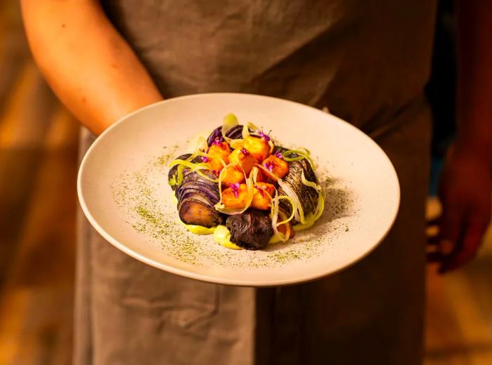 A server presents a dish garnished with fried fritters.