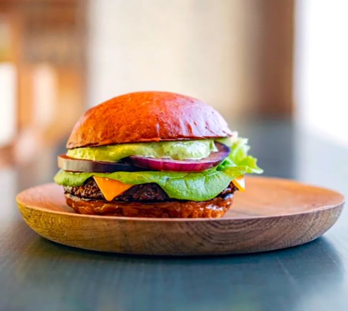 A hearty veggie burger topped with vibrant green sauce and a variety of toppings.