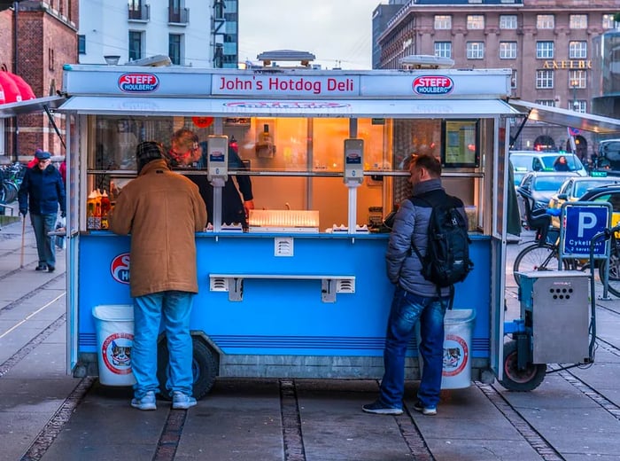 Patrons gather at a street cart, eagerly purchasing hot dogs.