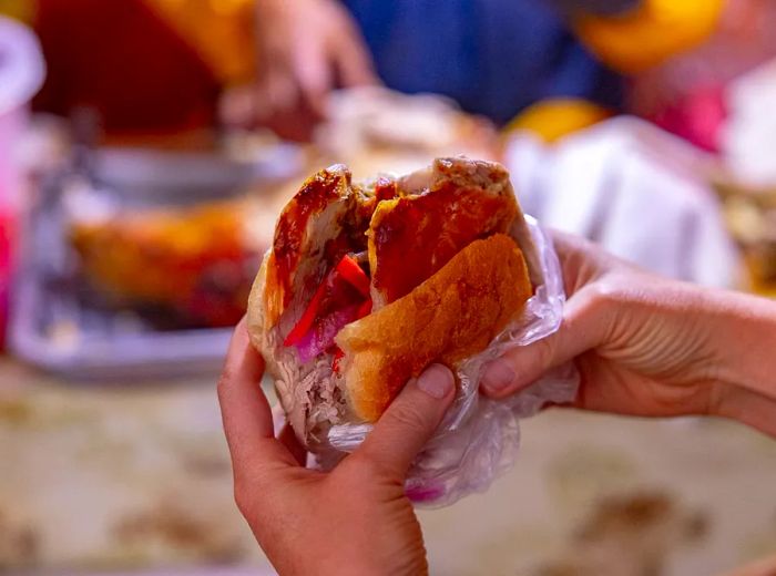 Hands holding a sandwich stuffed with meat.