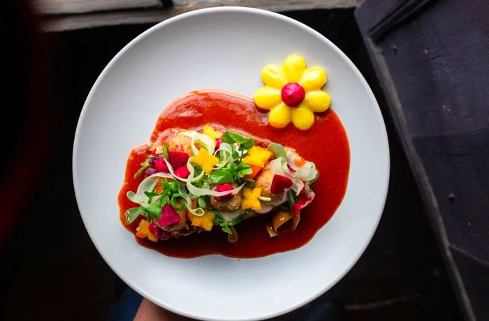 An overhead view of a dish adorned with vibrant garnishes and sauces, finished with a flower-shaped decoration.