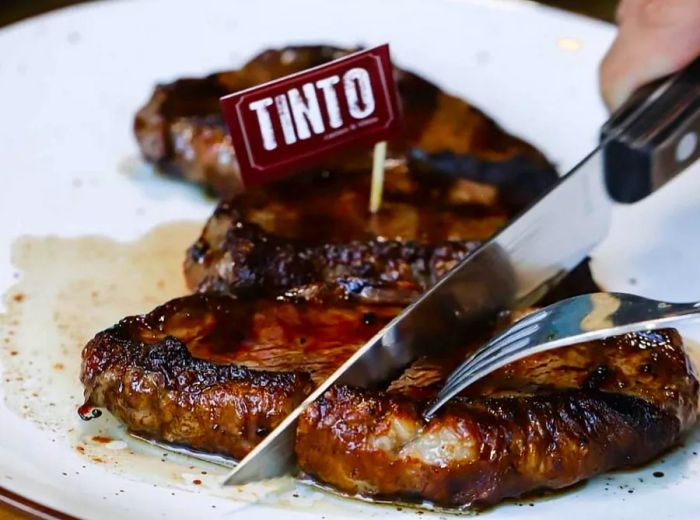 A patron slices into a steak, proudly marked with a little toothpick flag labeled Tinto.