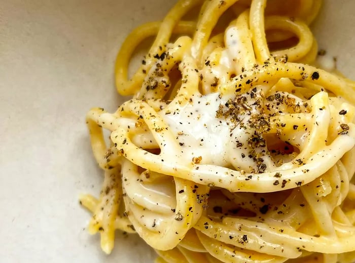 A close-up view of a bowl of pasta garnished with visible flecks of pepper and cheese.