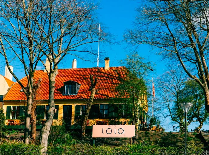 A hillside restaurant with a tiled roof, scattered outdoor tables among the trees, and a swirling sign that reads Lola.