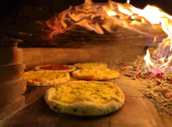 Multiple pizzas baking in a blazing oven.