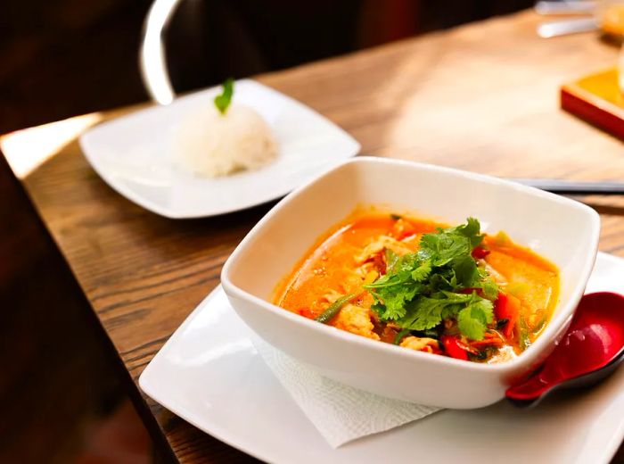 A bowl of red curry accompanied by various ingredients.