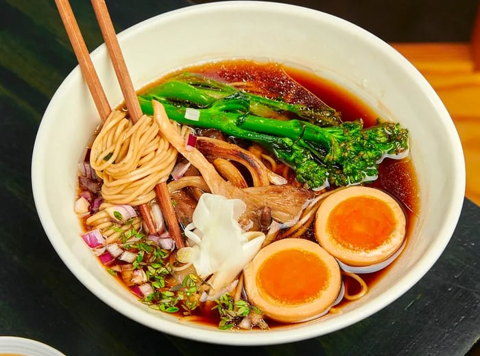 A vibrant bowl of ramen featuring a boiled egg, mushrooms, broccoli rabe, and an assortment of other chopped ingredients.