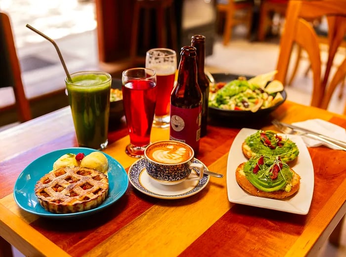 A table set with a fruit-filled waffle, an avocado dish, various drinks, and coffee.