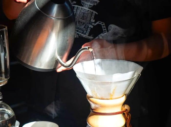 A barista skillfully pours hot water into a Chemex brewer.