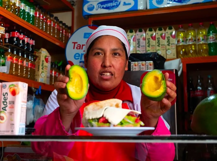 A vendor proudly displays avocado halves alongside a sandwich.