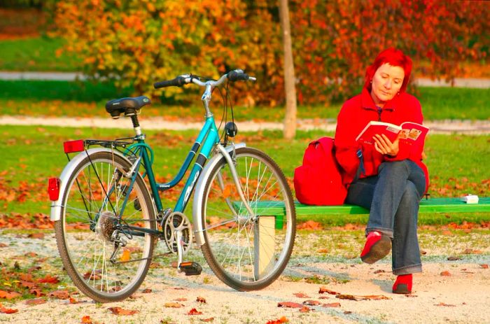 A woman sits on a bench in Park Tivoli, reading while her bike rests beside her in Ljubljana, Slovenia.