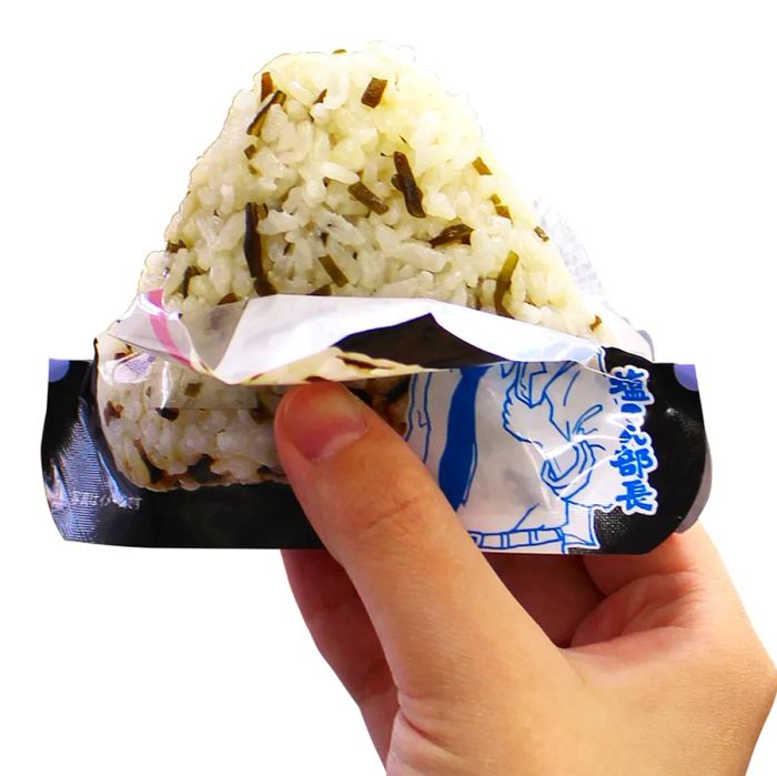 A hand lifts an onigiri that is partially unwrapped.