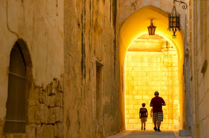 A father and son walk through an archway in Mdina, Malta, captured in silhouette.