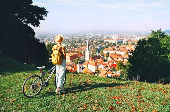 A woman stands beside her bike, gazing down at the red rooftops of Ljubljana from the castle grounds.